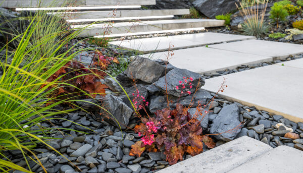 Closeup of Dark Grey Decorative Garden Stones and Pebbles Along the Concrete Slab Pathway. Residential Garden Design Ideas.