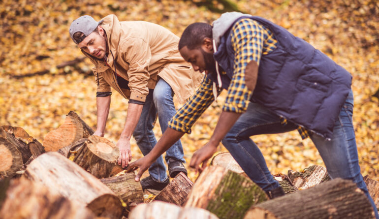 Two young men tourists near a heap of dry stumps in autumn forest